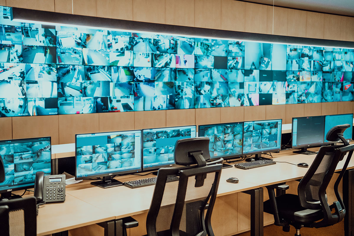 An empty security operations centre at night, rows of monitors displaying camera feeds above a bank of unoccupied workstations