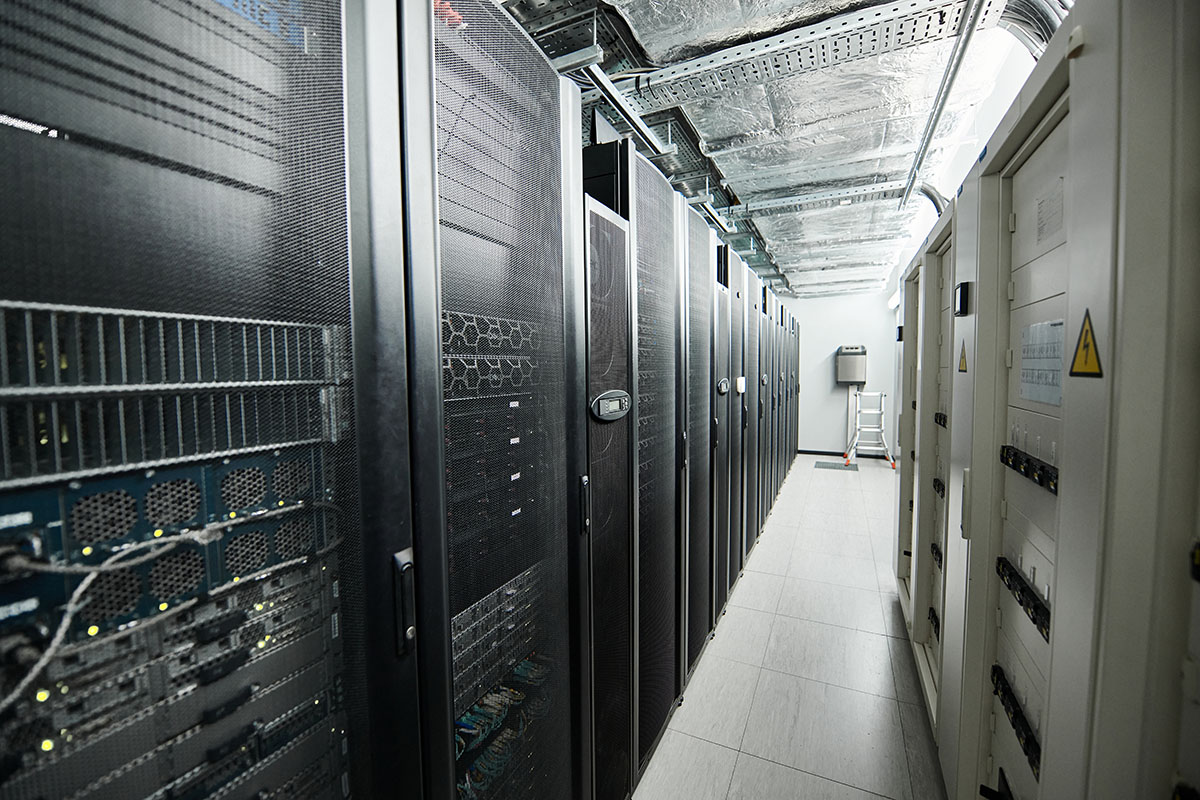 A dark data centre aisle lined with server racks and cabling, with no people in frame