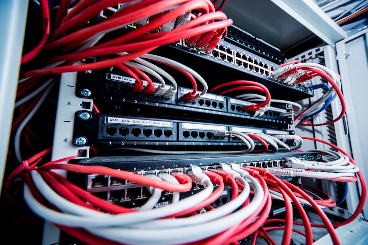 Network switches and patch panels in an equipment rack, densely connected with red and white ethernet cables and labelled port numbers